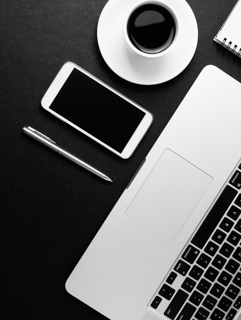 laptop, pen, note pad, smart phone and cup of coffee on black ba